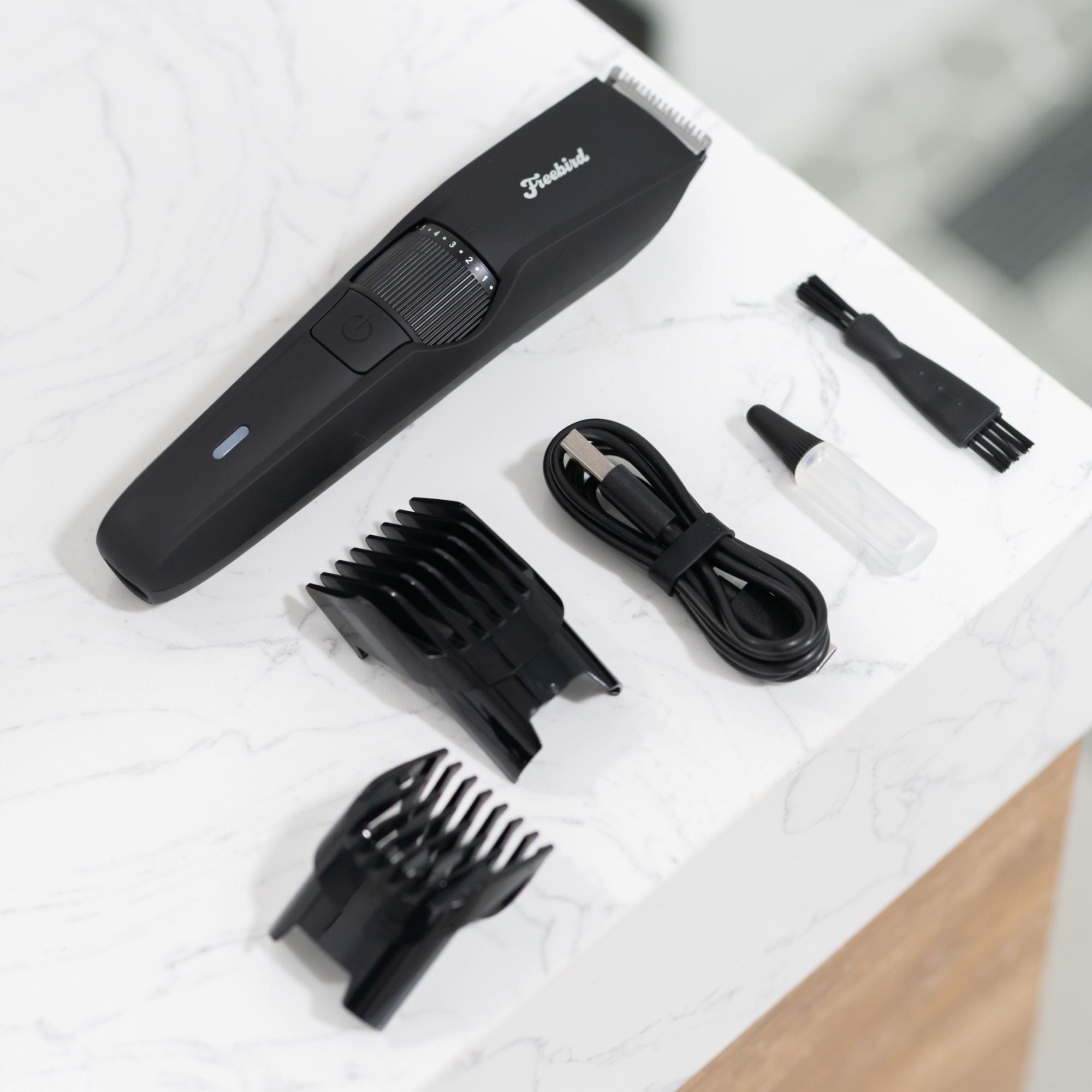 Freebirds BeardSeries Trimmer, with attachments, brush, cable, and oil bottle, on a white marble surface.