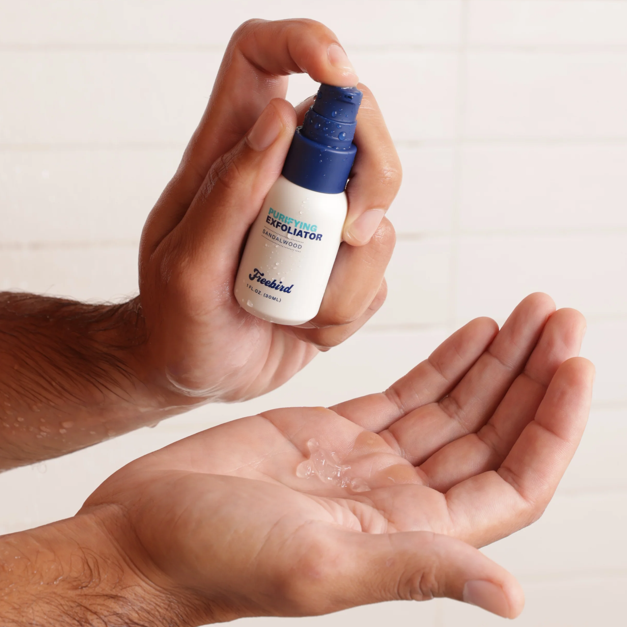 An individual applying Freebird's Purifying Scalp Exfoliating Scrub from a blue and white bottle onto their palm to softly eliminate dead skin cells, revealing a baby-smooth scalp.