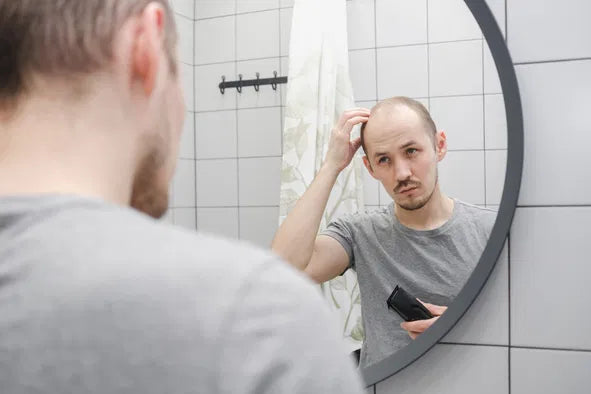 bald man looking at mirror holding electric shaver