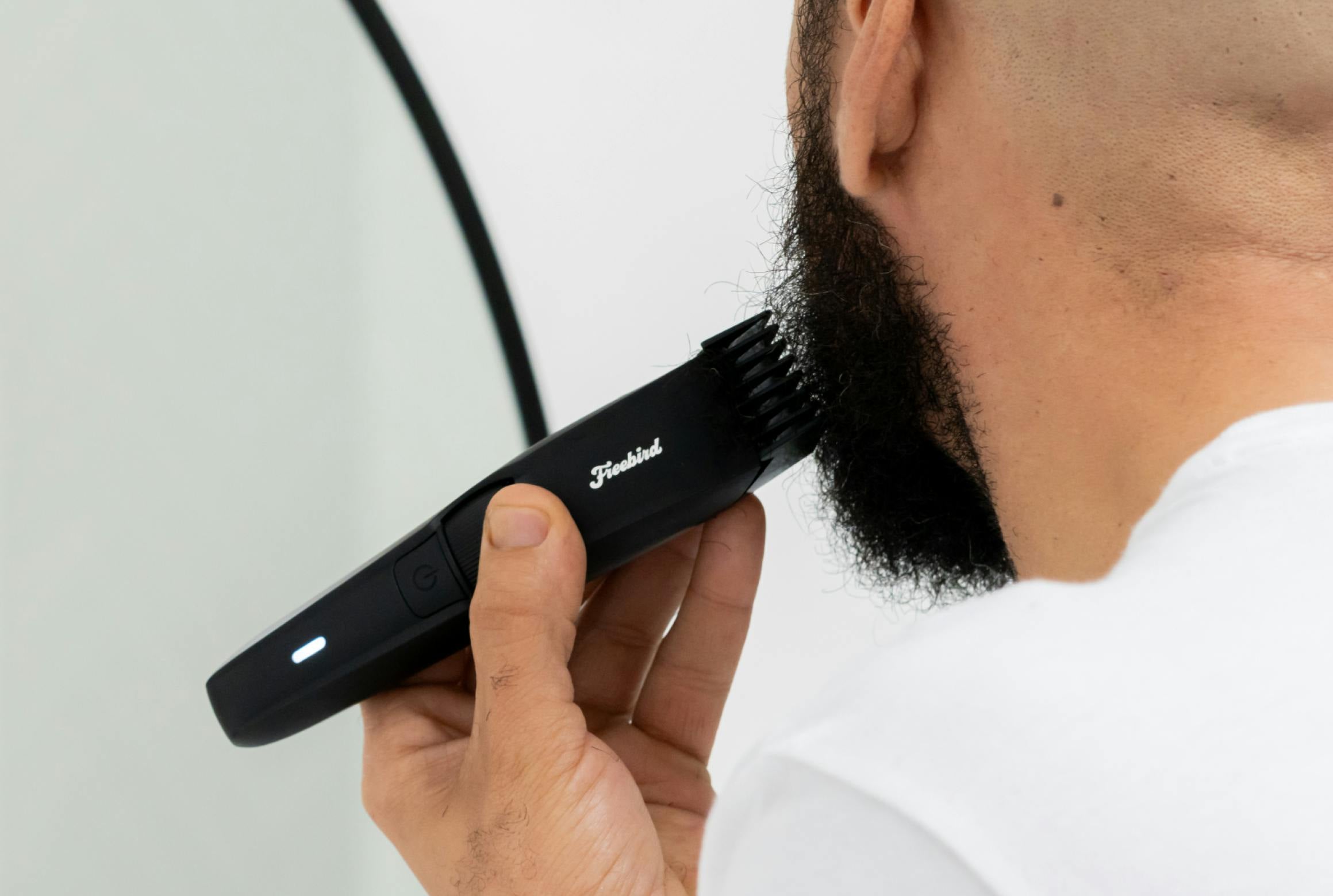 Person using an electric trimmer to shape their beard in front of a mirror.