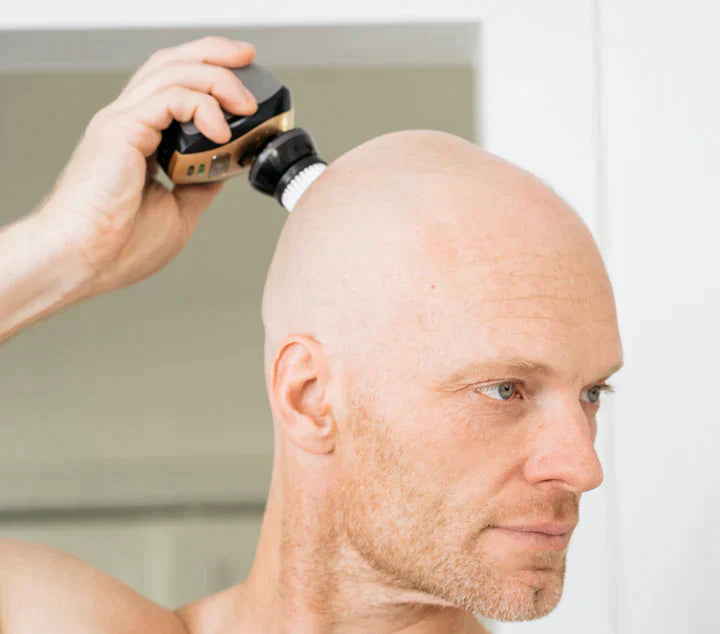 A man shaves his bald head with the Freebird FlexSeries® Shaving Kit featuring ScalpSafe™ Technology in front of a mirror.