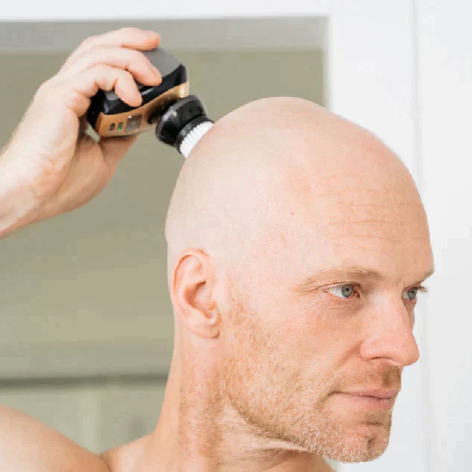 A man confidently shaving his bald head with the FlexSeries® Shaving Kit from Freebird, equipped with ScalpSafe™ Technology, in a bright room.