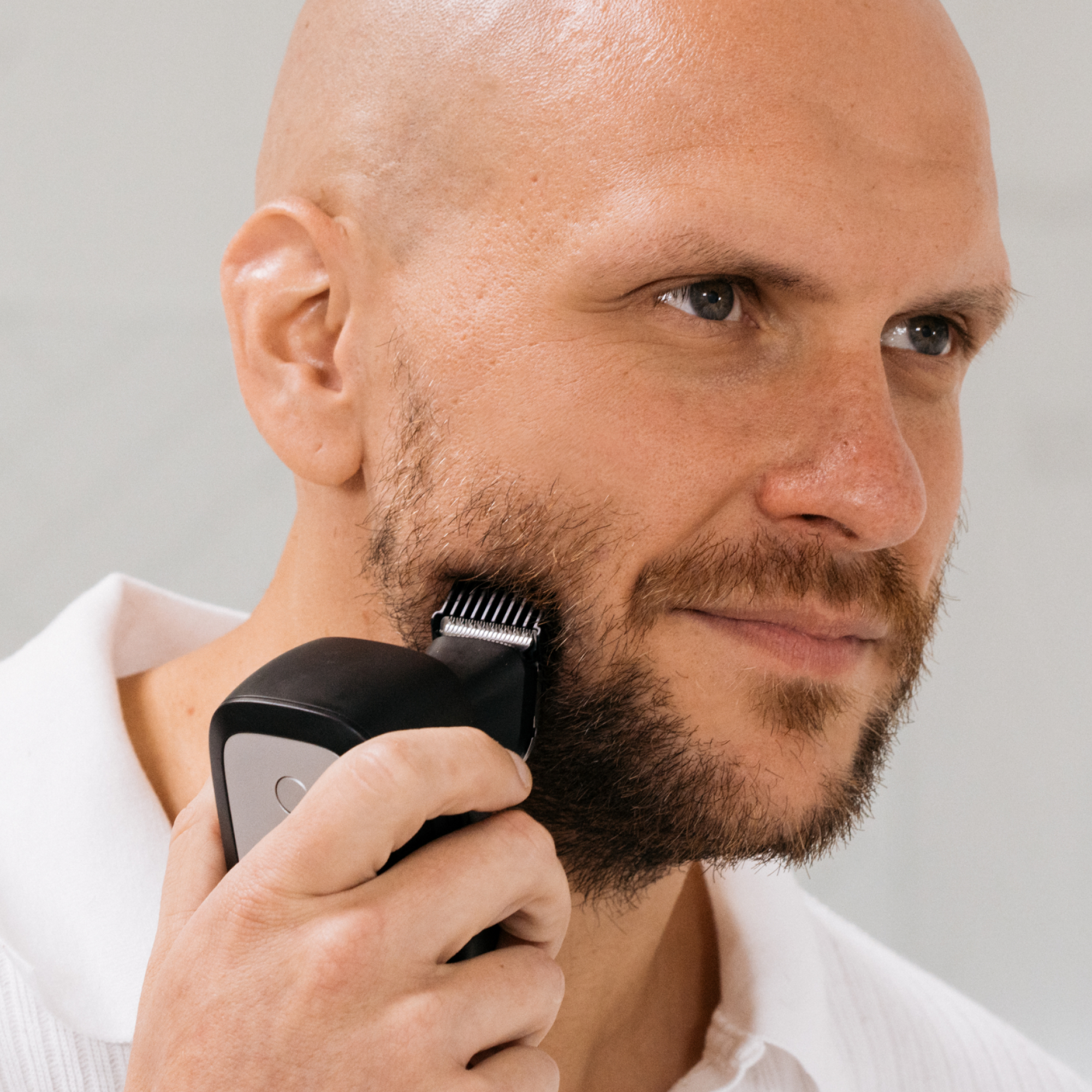 A man in a white shirt uses the FlexSeries® Pro Shaving Kit by Freebird, featuring a Four-Blade System, to groom his beard in a neutral setting.