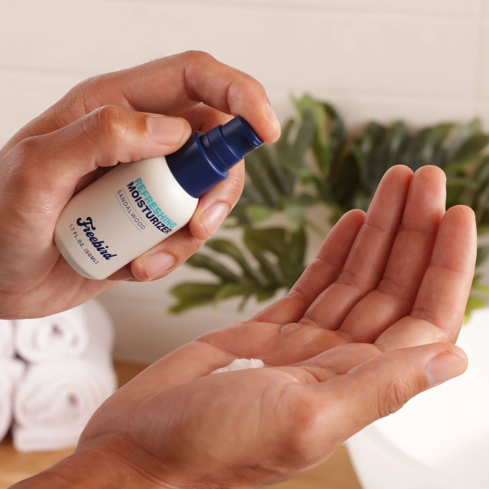 Hands dispensing Freebird's Refreshing Scalp Moisturizer from a pump bottle into the palm, infusing the skin with hydrating benefits, while a leafy plant blurs softly in the background.