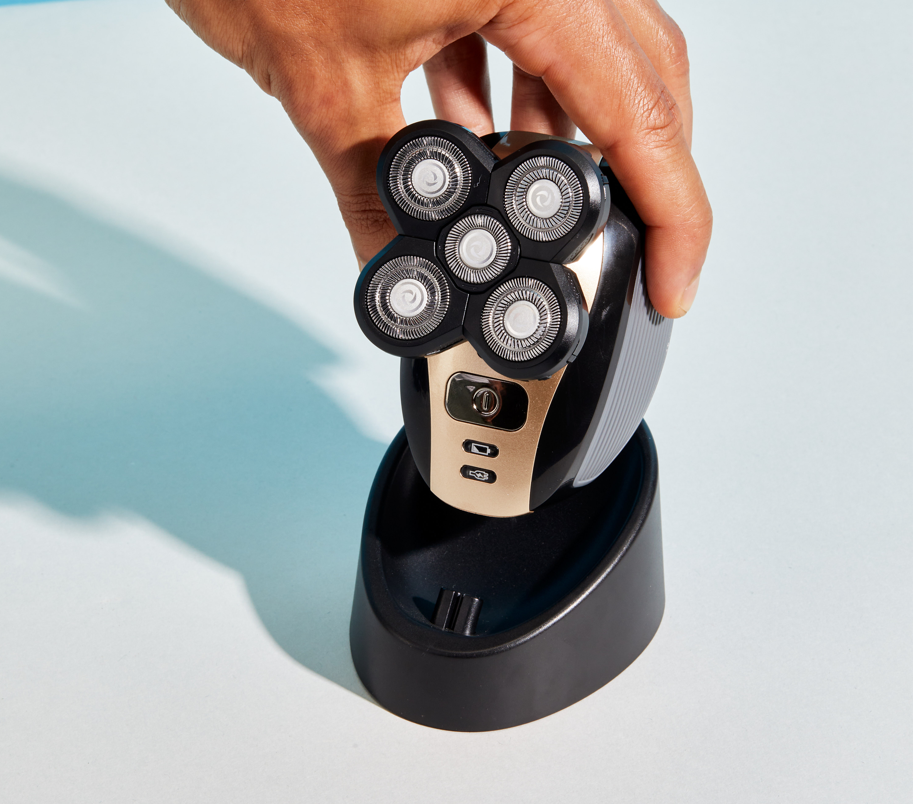 A hand holds a sleek black and gold FlexSeries™ electric shaver by Freebird, featuring five circular blades, elegantly displayed on its FREE charging dock.
